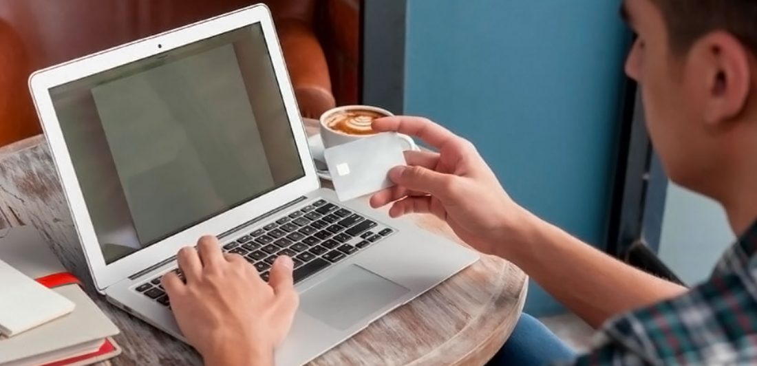 Image of man with a cup of coffee making an online payment on his laptop