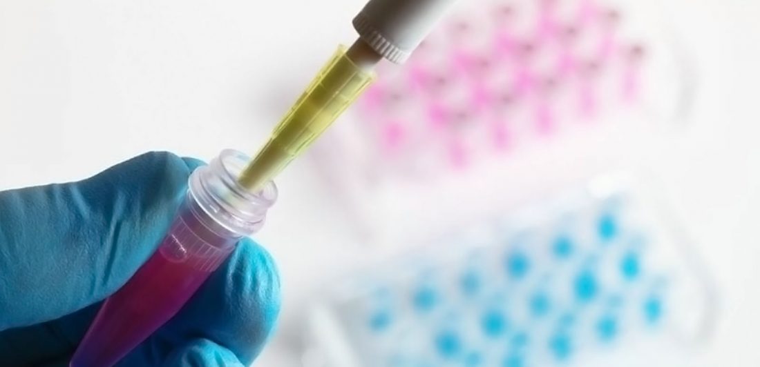 Up close image of a gloved hand filling a test tube with pink liquid