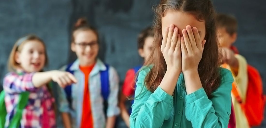 Image of young children bullying a girl who has her hands covering her face