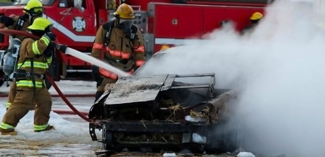 Image of vehicle fire with firefighters spraying the vehicle with a hose