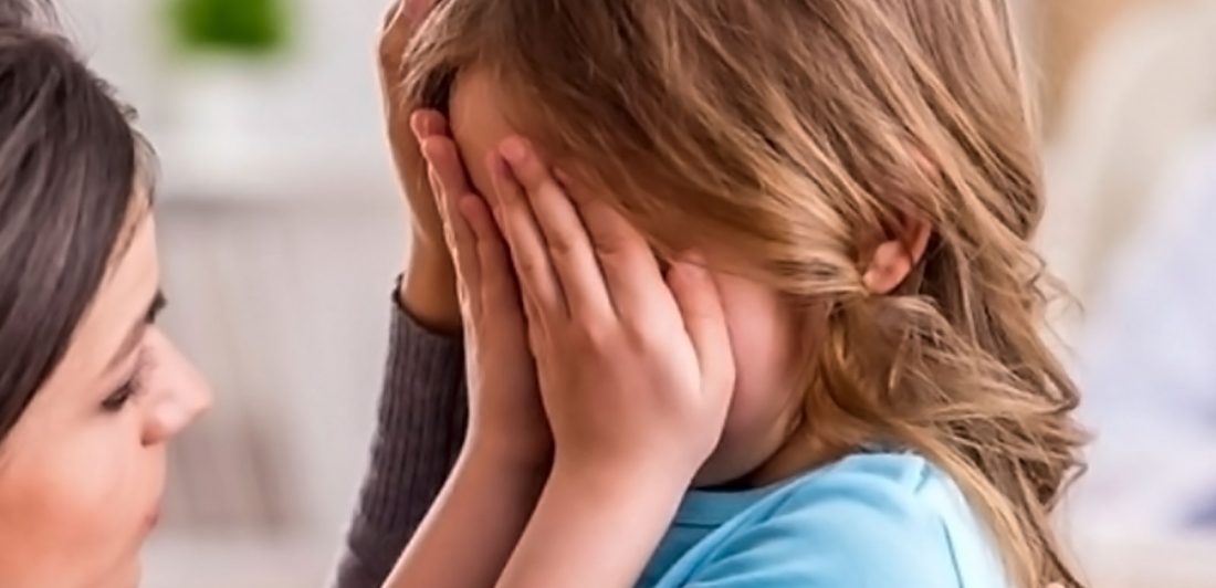 Image of a scared child with their face covered and a woman comforting them