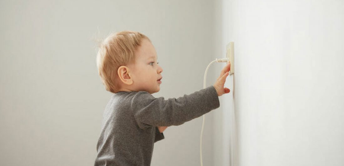 Image of a young toddler touching an electrical outlet with cord plugged in