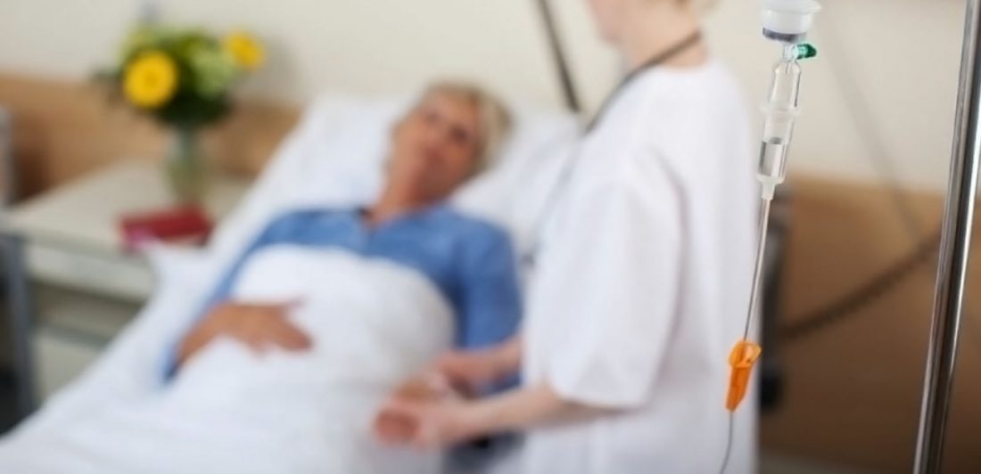 Image of medical professional checking on a patient in bed with an IV drip in the foreground