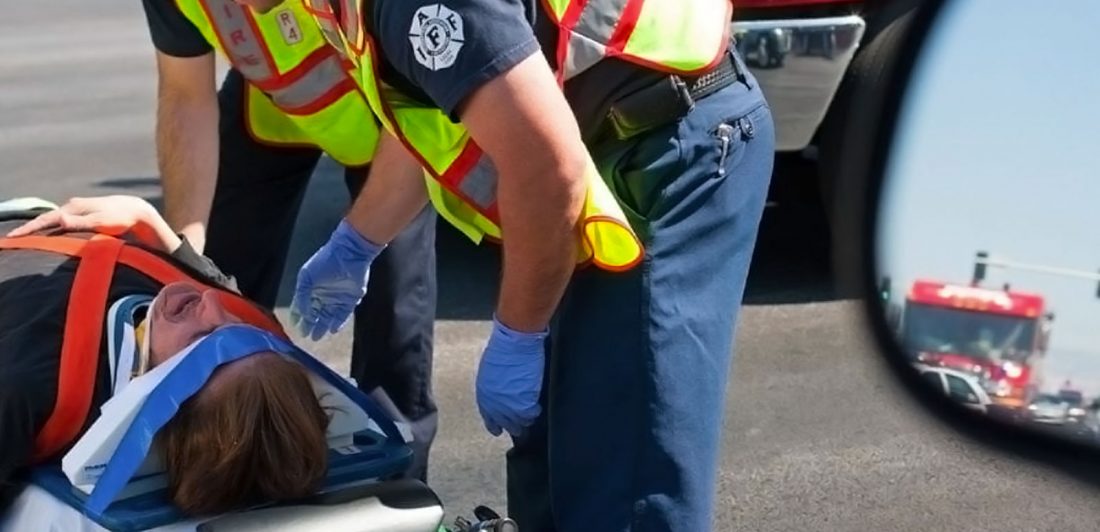 Image of person in pain on a stretcher with head restraint being cared for by paramedics