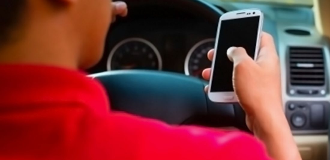 Image of person using their cell phone while behind the wheel of a vehicle