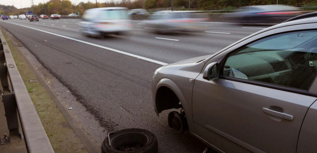 Image of car with missing tire on shoulder of a busy highway