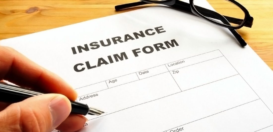 Image of hand filling out insurance claim form with a pen and sunglasses nearby