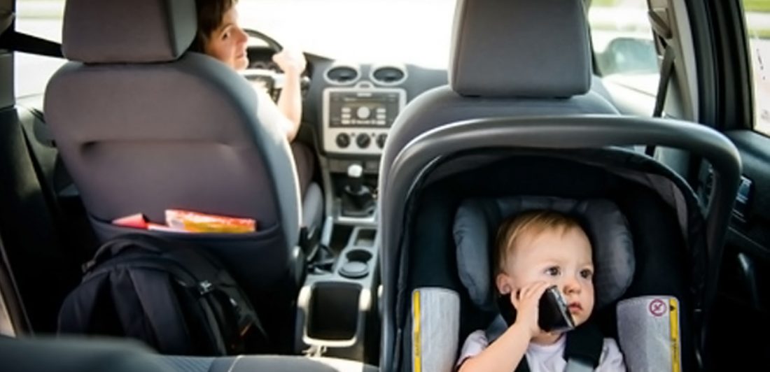 Image of woman driving with baby in a rear facing car seat pretending to talk on the phone