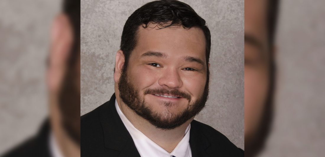 Image of Man with dark hair and beard wearing a black suit, black tie, and white button up shirt