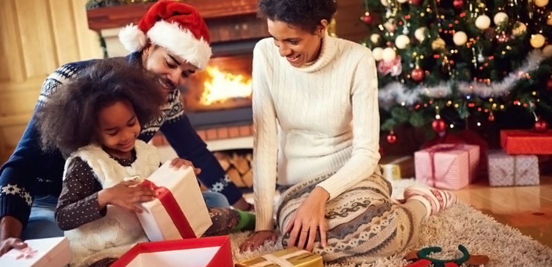 Image of happy family opening gifts by a Christmas tree and fireplace