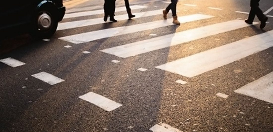 Image of pedestrian feet walking across a crosswalk with a car waiting