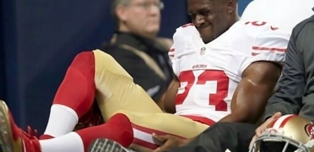 Image of an injured Reggie Bush in a red, white, and gold football uniform holding his leg in pain