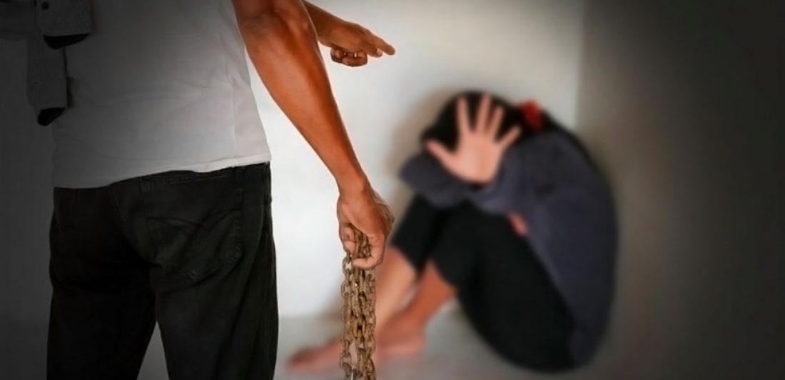 Image of man holding a chain pointing at a scared woman in a corner who is covering her face and holding up her hand