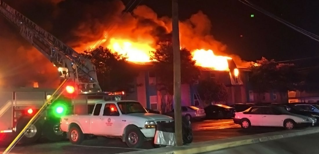 Image of a large apartment fire with vehicles and fire truck