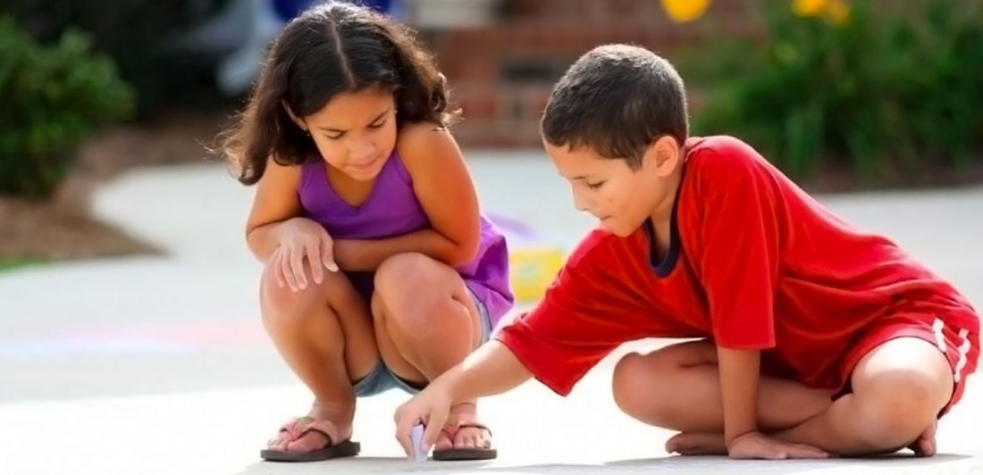 Image of two children drawing outside with sidewalk chalk