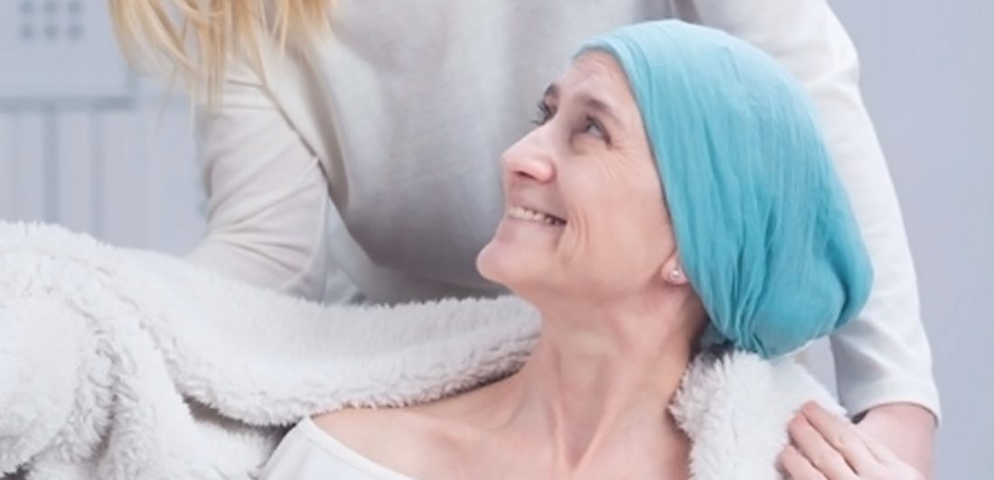 Image of a cancer patient in a head wrap being covered with a cozy blanket by someone