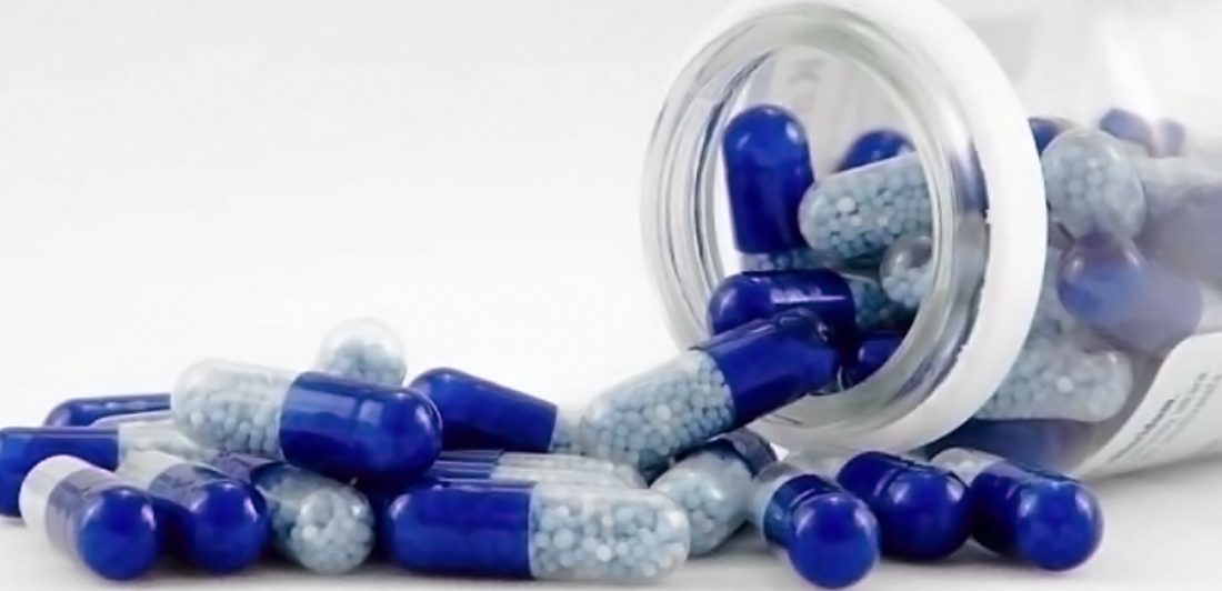 Image of blue capsule pills spilling from a clear bottle