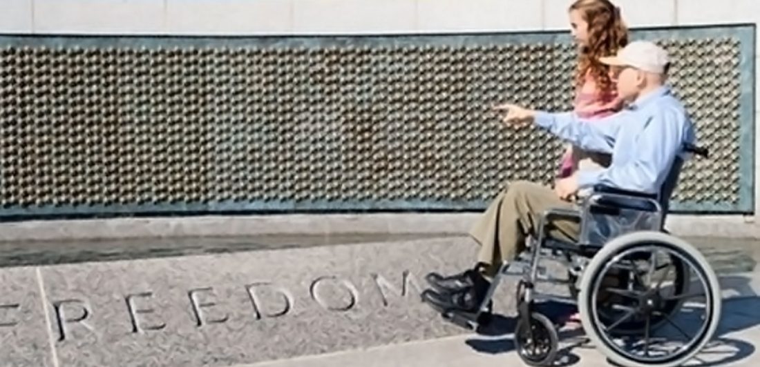 Image of a veteran in a wheelchair visiting a war memorial with a young girl