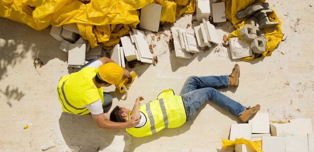 Image of injured construction worker in safety gear on a worksite being assisted by coworker