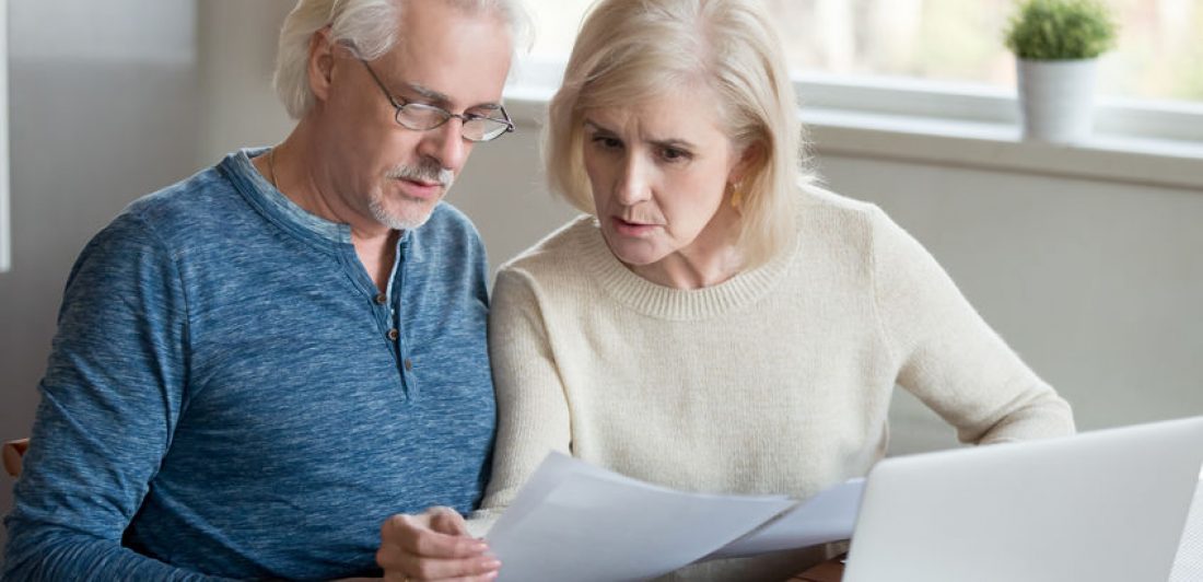 Senior couple reading paperwork in front of laptop