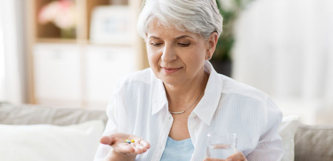 Image of senior woman taking medication with a glass of water